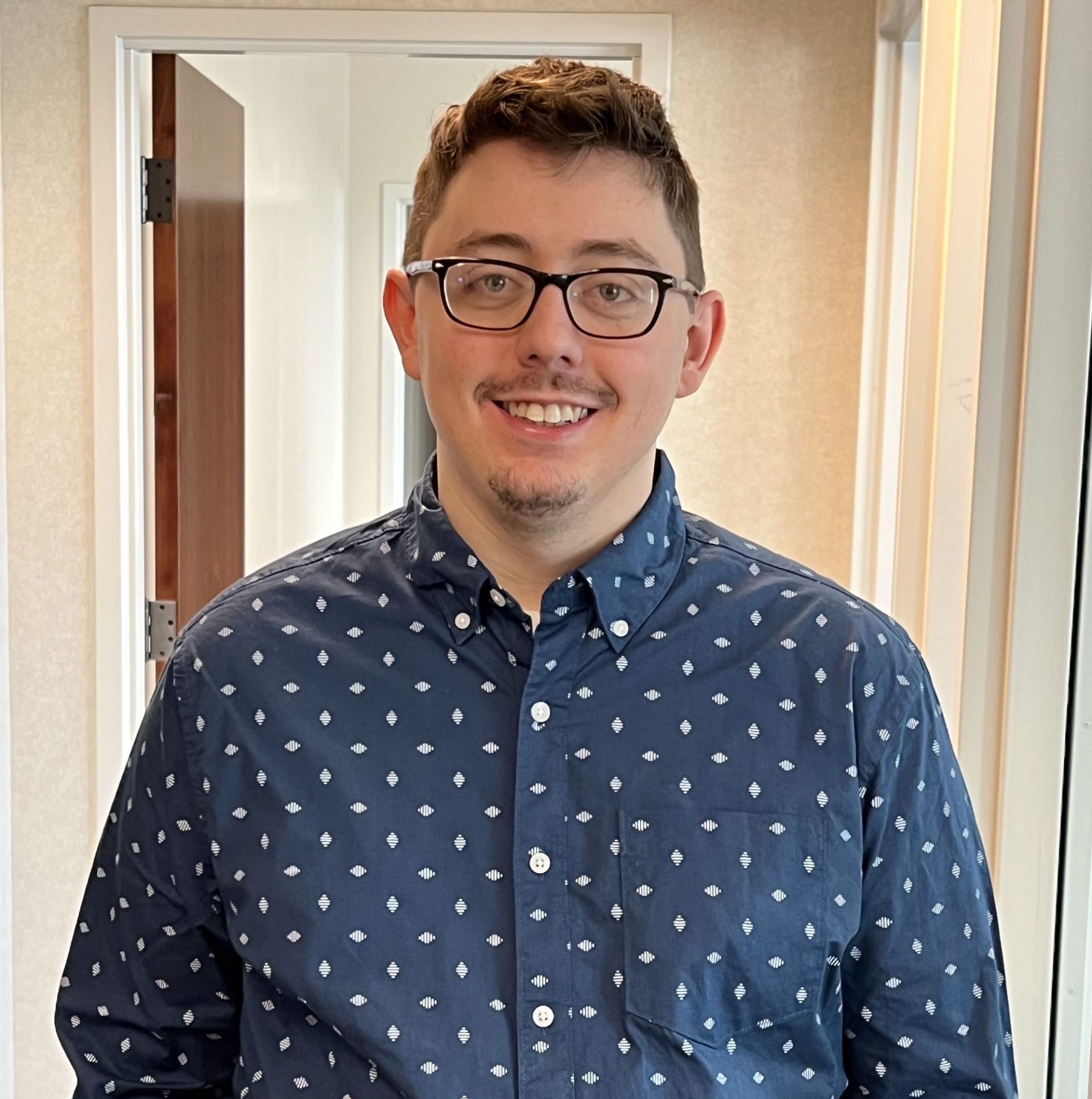 A smiling male professional wearing glasses and a patterned shirt, representing human-centered intelligence in enterprise AI.