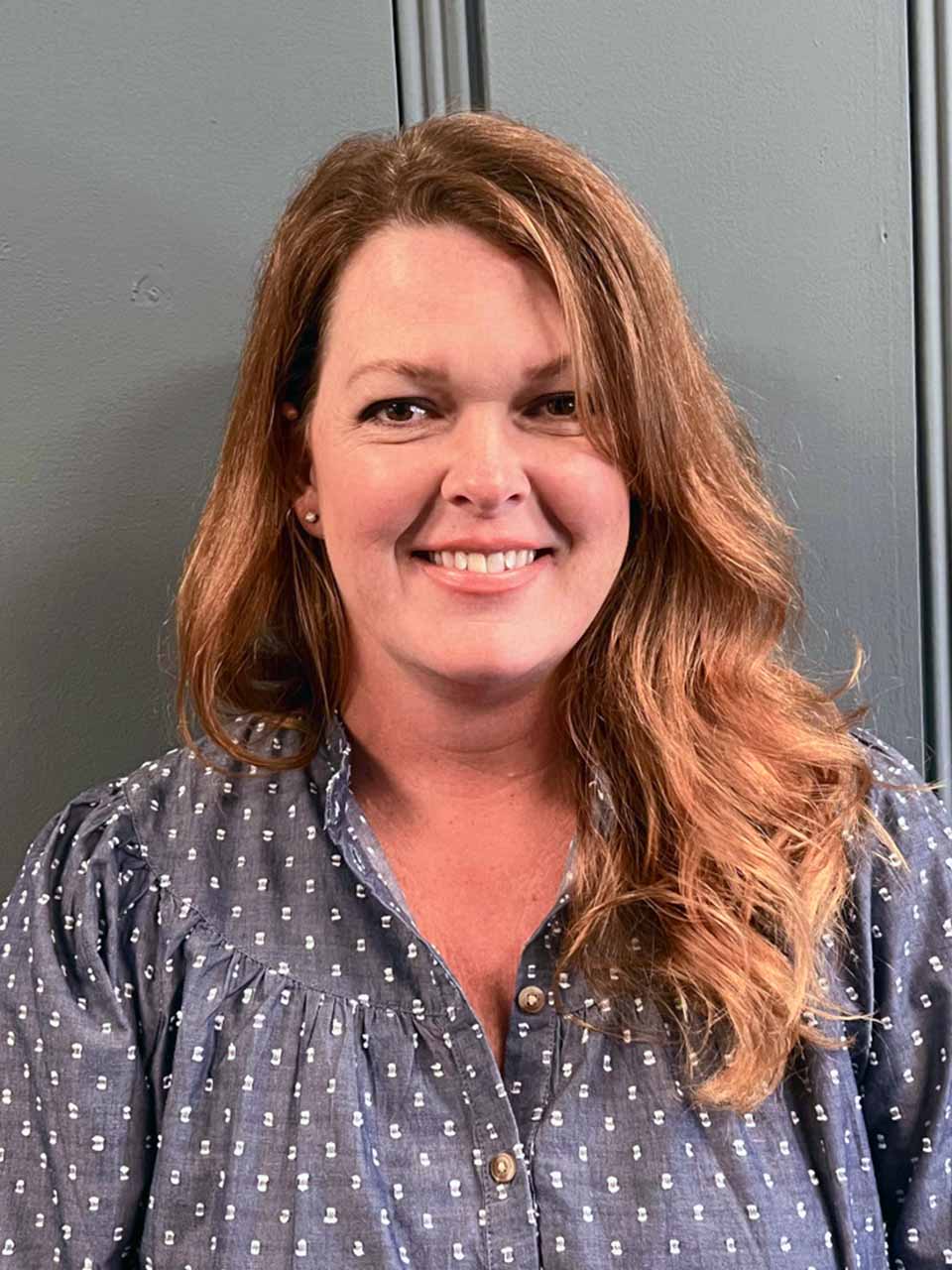 Professional woman with a warm smile, red-brown hair, and patterned shirt, part of Mined XAI's human-in-the-loop AI team.