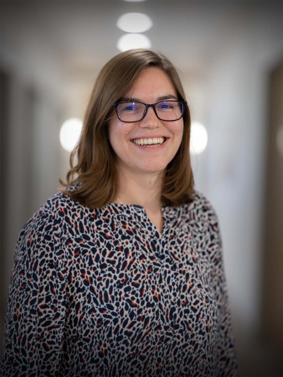 A smiling professional woman wearing glasses, reflecting the human-centered approach of Mined XAI's explainable AI solutions.