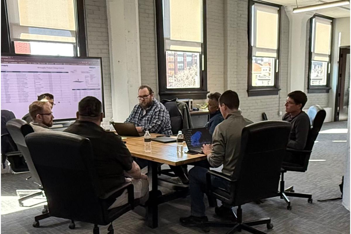 A team of professionals collaborating around a table, reviewing enterprise AI and supply chain data on a large monitor, lever